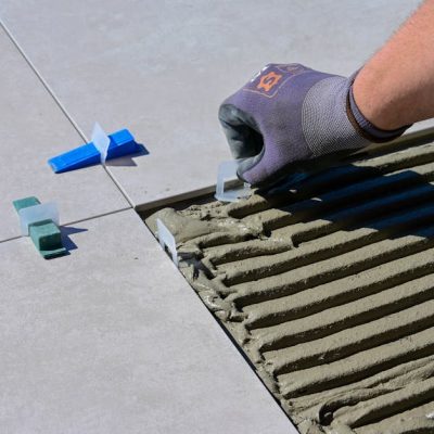 Detailed view of gloved hand aligning tiles with levelers and spacers during construction.