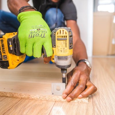 Man using a power drill for home improvement on a wooden floor with precision.