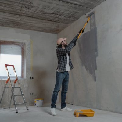 A man painting an interior wall with a roller during a home renovation project.